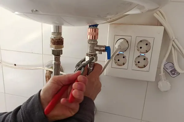 Fontanero sustituyendo pieza de termo eléctrico con llave inglesa en baño